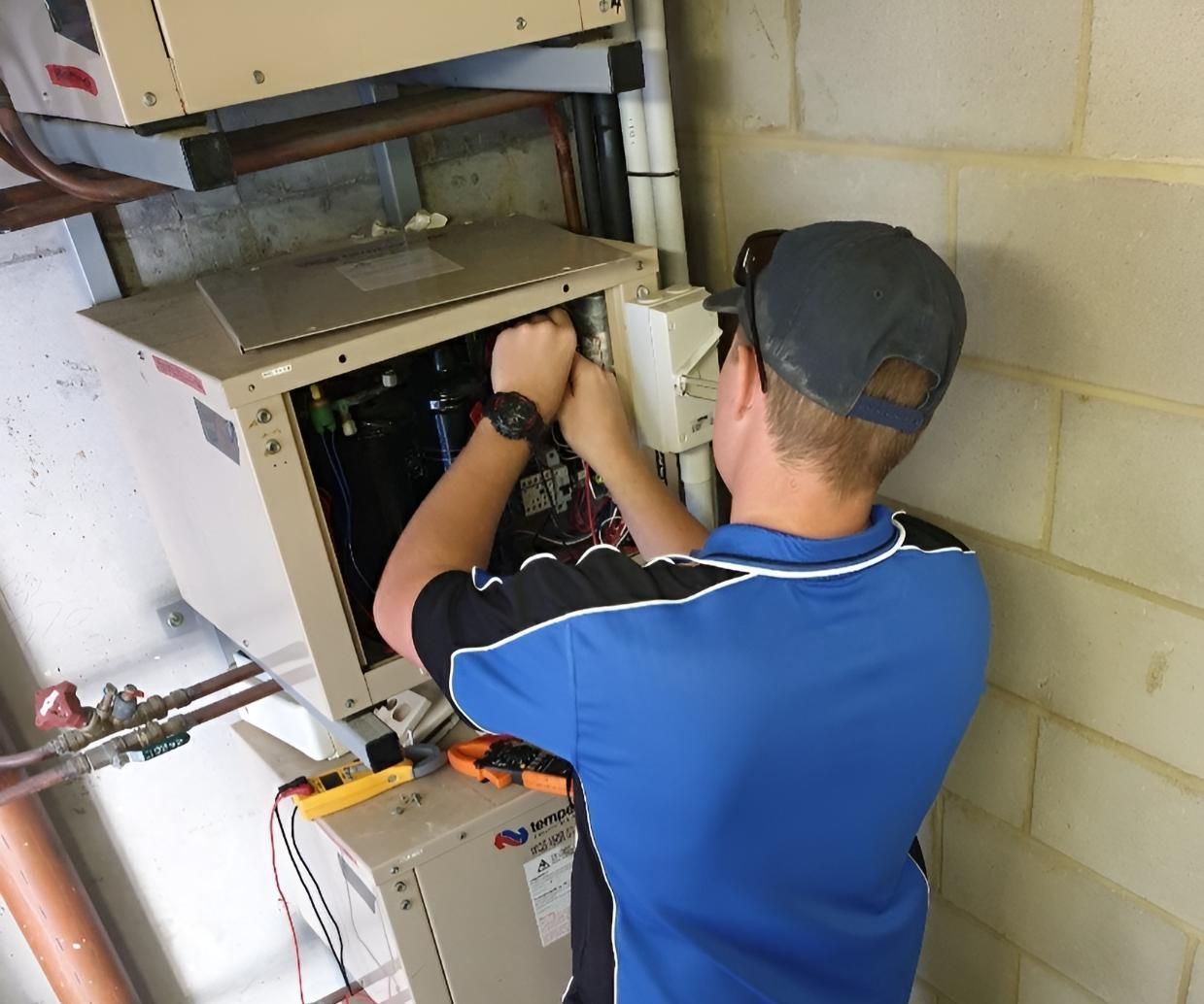 A Man in a Blue Shirt is Working on an Electrical Box — Atmosphere Air Conditioning & Refrigeration In Taylors Beach, NSW