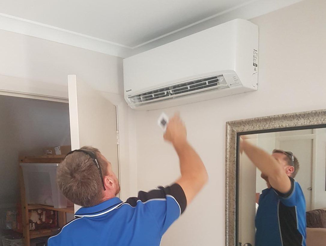 A Man is Installing an Air Conditioner in a Living Room — Atmosphere Air Conditioning & Refrigeration In Taylors Beach, NSW