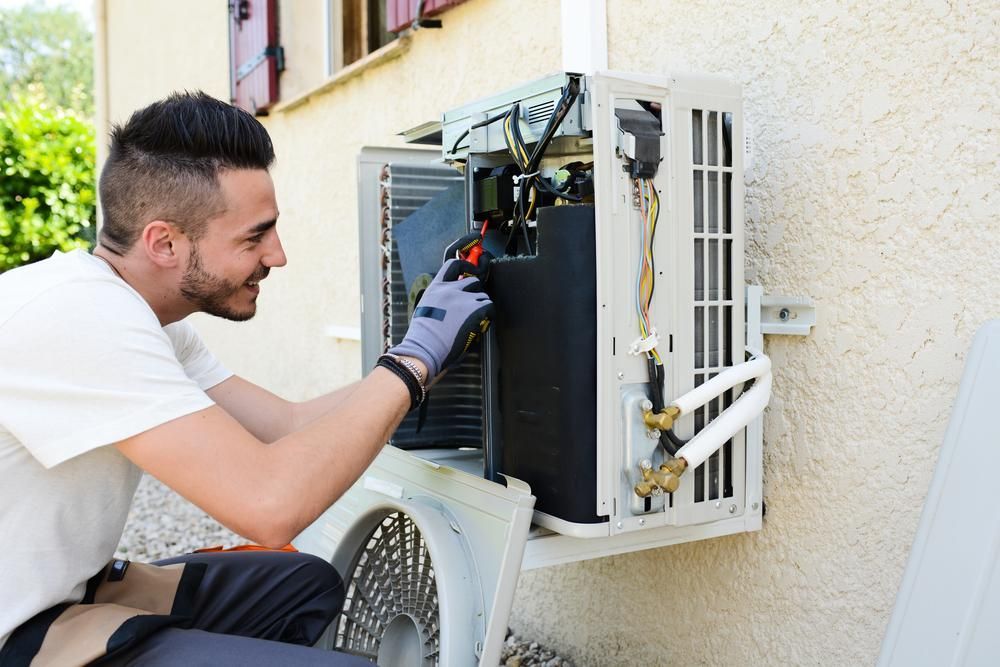 A Man is Fixing an Air Conditioner— Atmosphere Air Conditioning & Refrigeration In Lemontree Passage, NSW