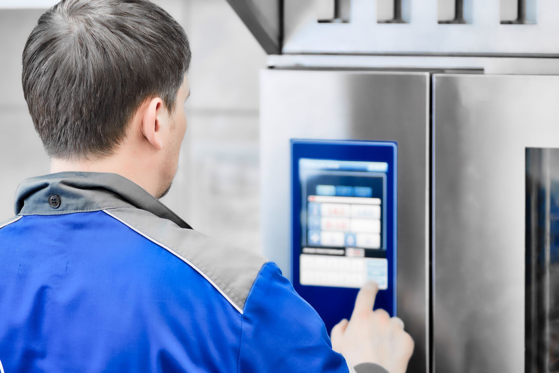 A male technician is operating an industrial oven with a digital control panel.
