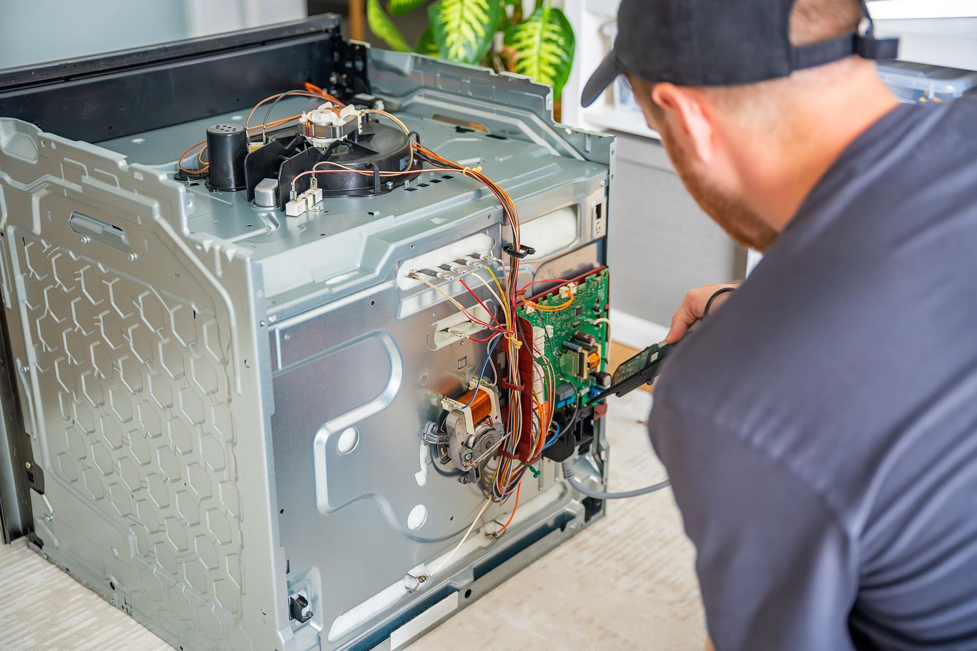 A technician is testing electronic components and wiring inside a disassembled electric oven.