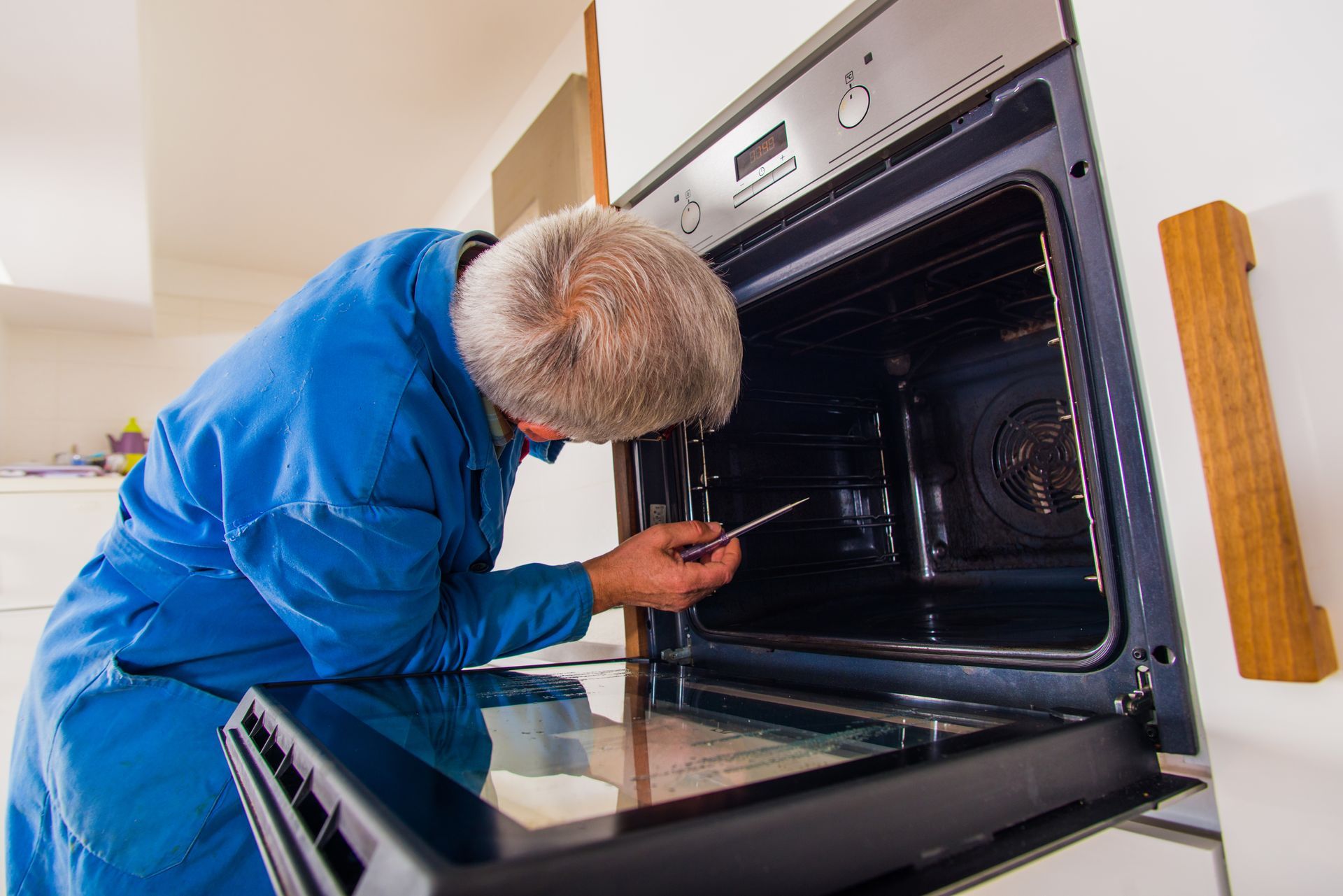 A technician wearing a blue uniform is repairing an oven, showcasing electrical appliance repair.