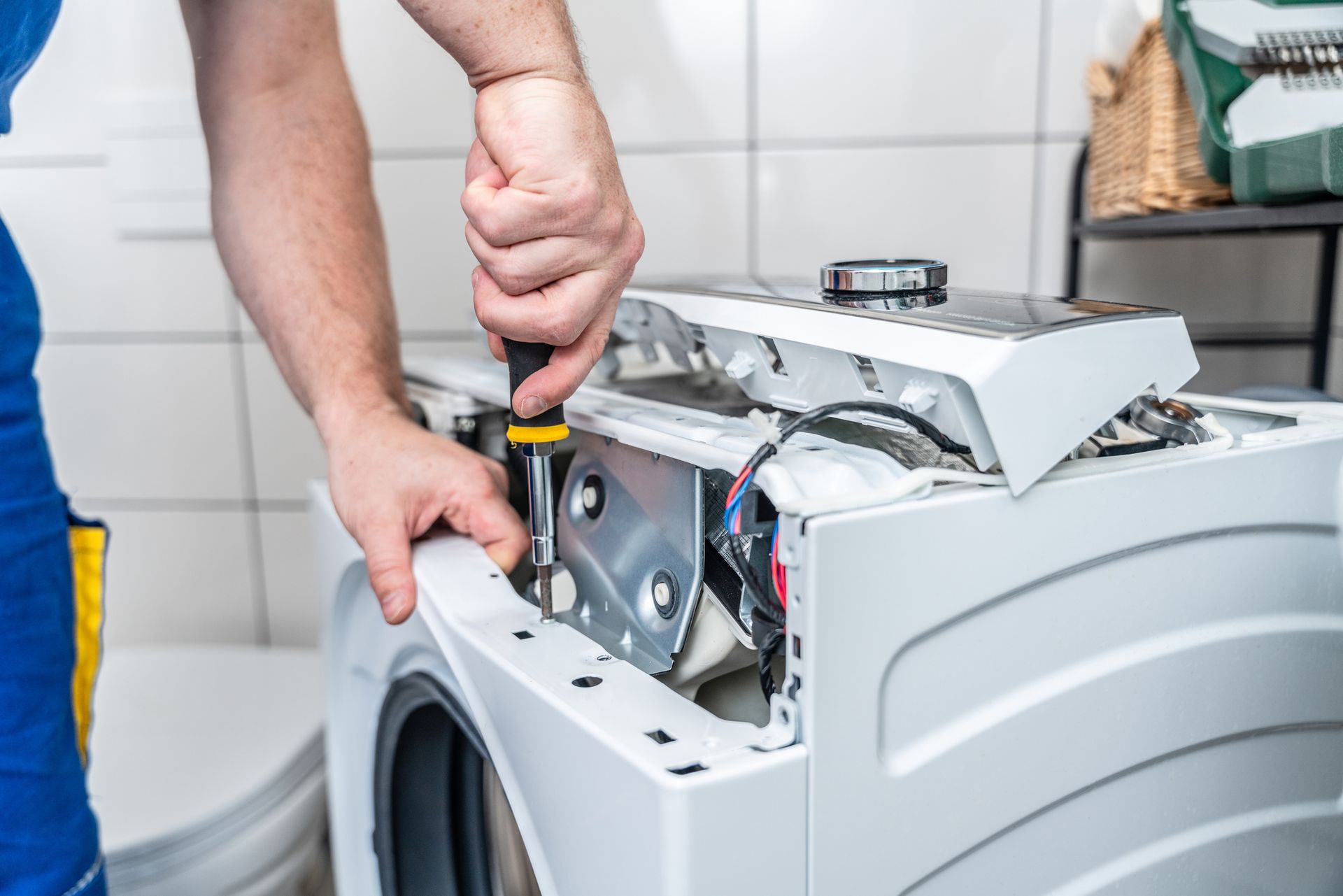 Person using a screwdriver to repair a washing machine.