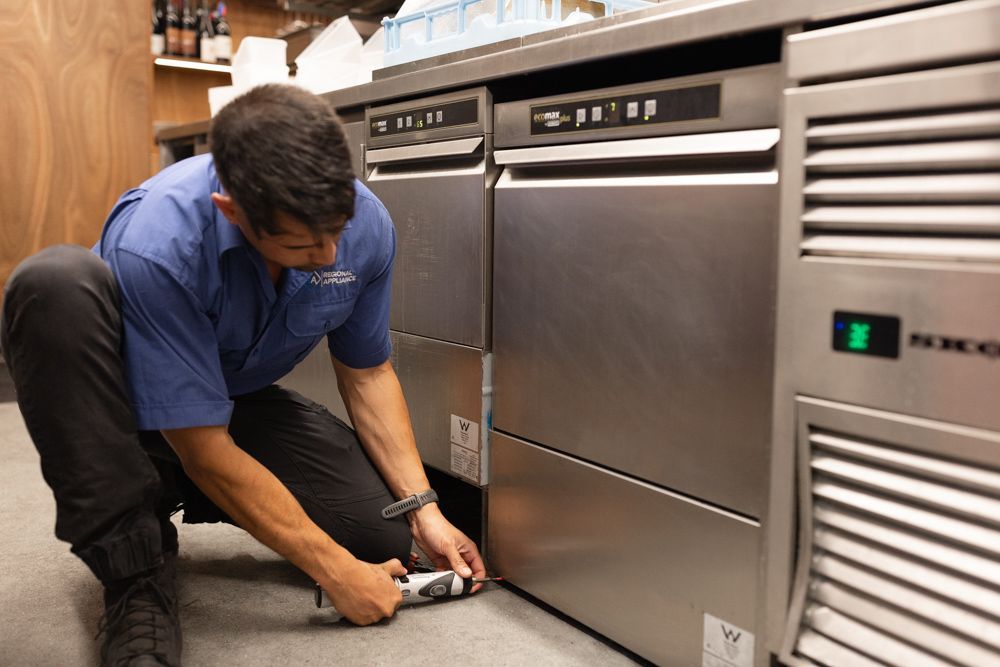 Regional Appliance & Electrical Services technician repairing a commercial dishwasher.