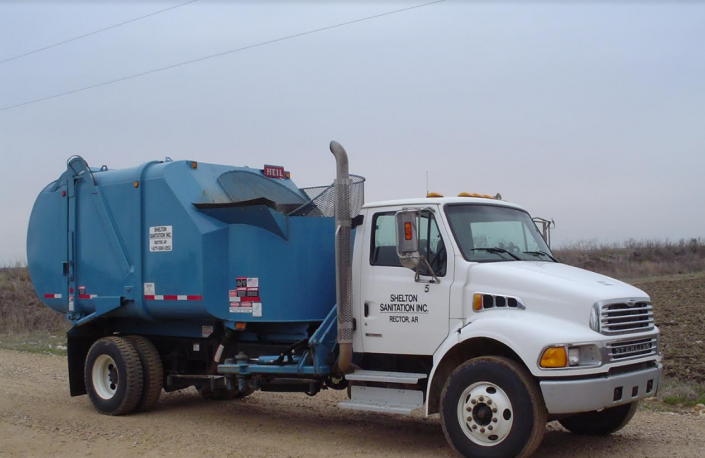 White cab garbage truck with blue rear container parked on a dirt road under a cloudy sky