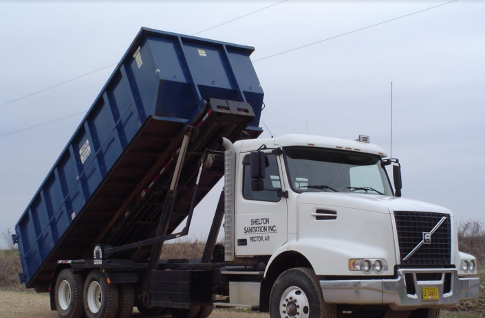 White dump truck tipping a blue container upward at a construction site