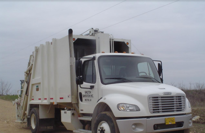 White garbage truck on a dirt road under a cloudy sky