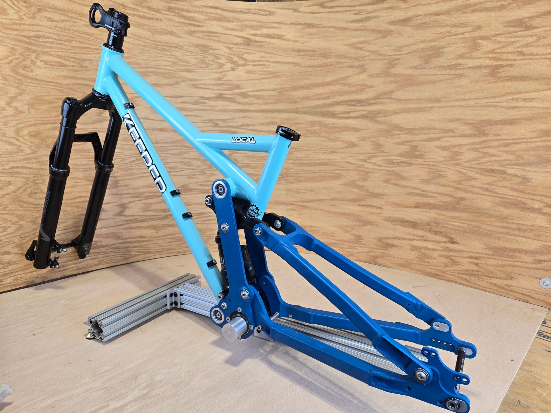 Light blue mountain bike frame with black front fork, on a stand.
