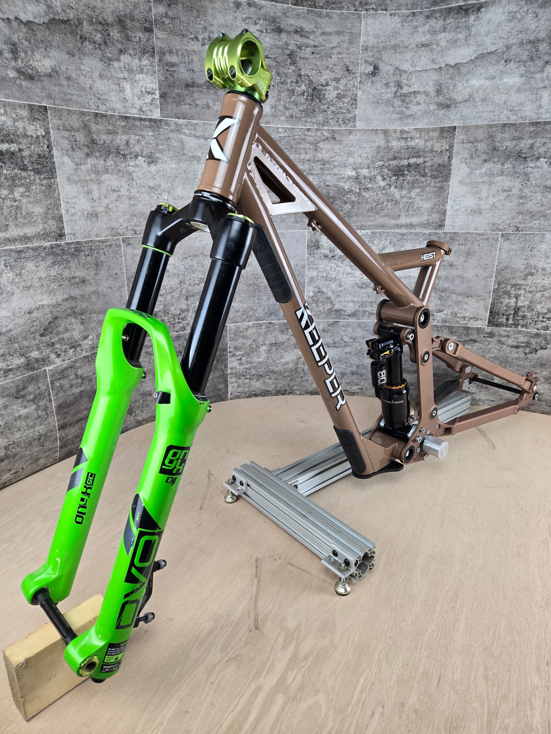 Brown and green mountain bike on a stand outdoors with a cornfield in the background.