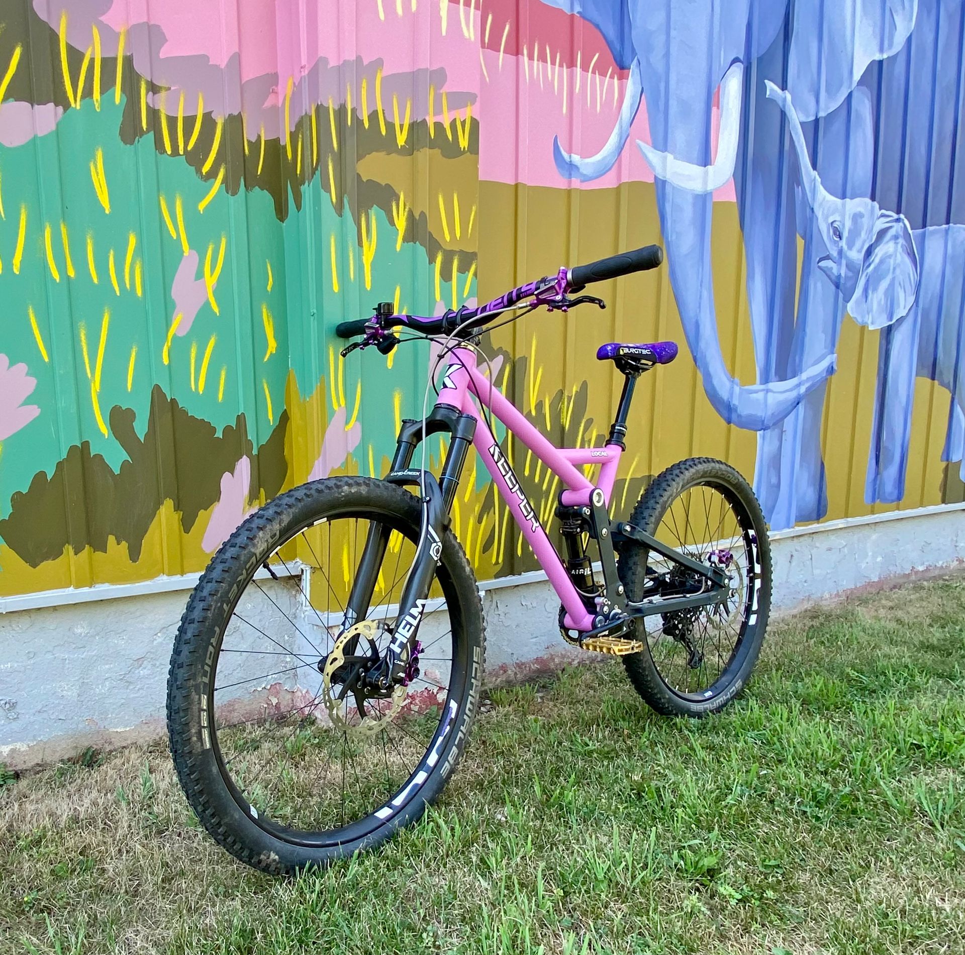 Pink and black mountain bike frame with fork and suspension; on a light surface.