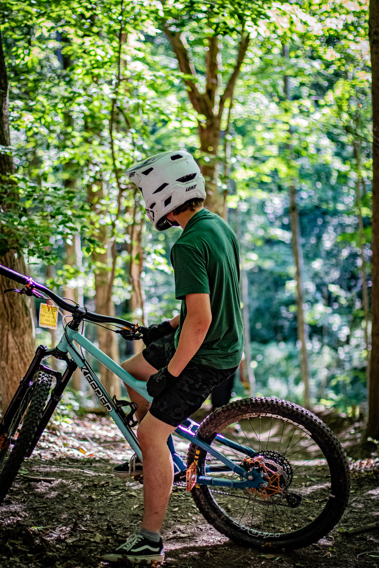 Person in helmet and green shirt on mountain bike in forest, resting.