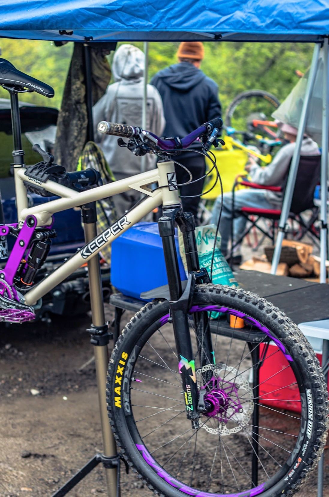 Tan mountain bike with purple accents, propped up outdoors, people in the background.