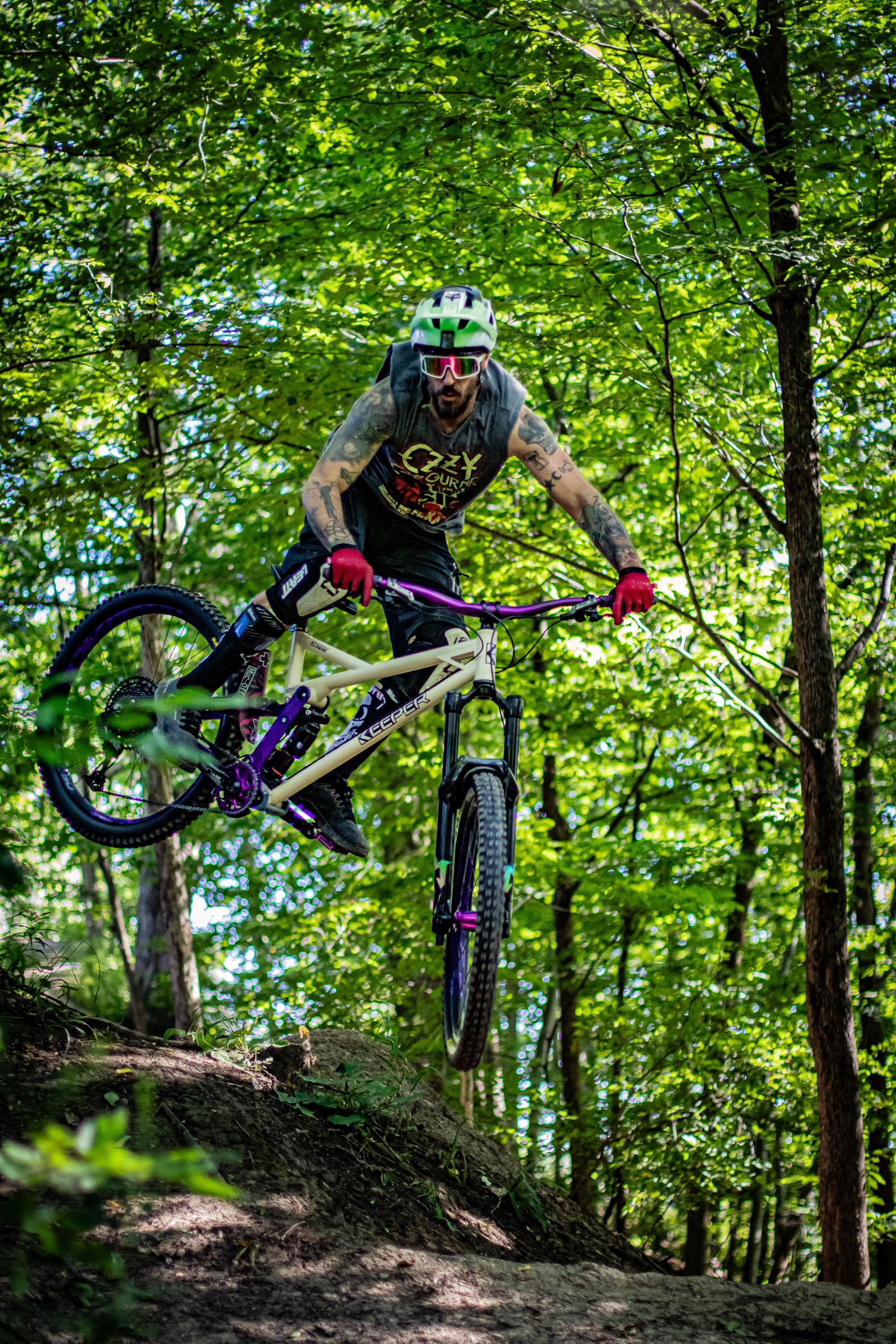 Mountain biker riding on a dirt trail in a forest, trees surround the rider, green shirt, sunlight.