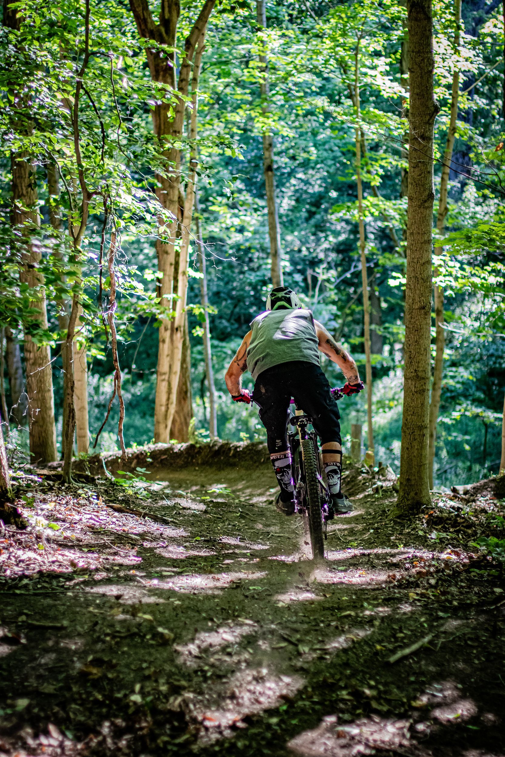 Mountain biker leans into a turn on a dirt trail in a forest, trees surround.