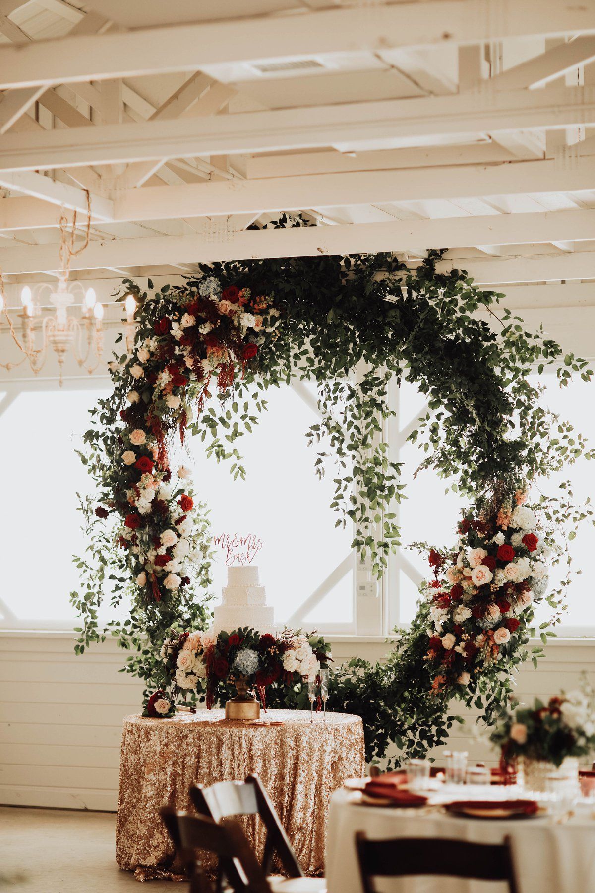 Wedding reception with round floral arch, decorated cake on sequin tablecloth.