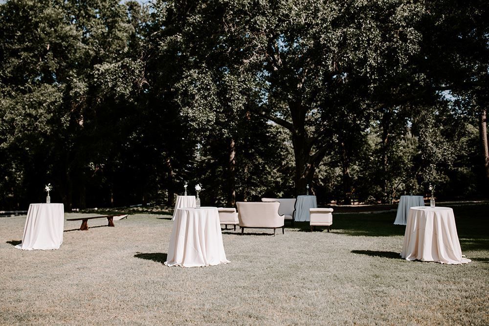 Outdoor reception with round tables draped in white, lounge seating, and trees.