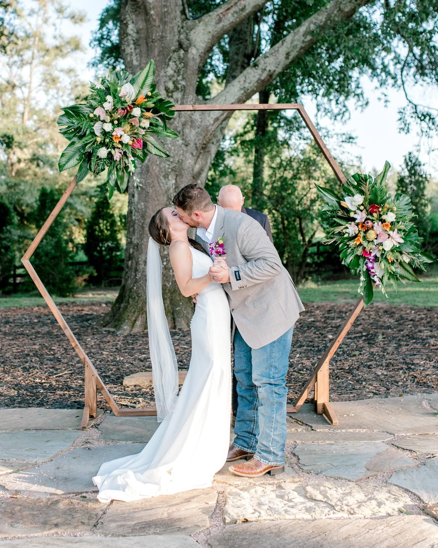 Couple kissing under a floral decorated hexagonal arch at a wedding ceremony.
