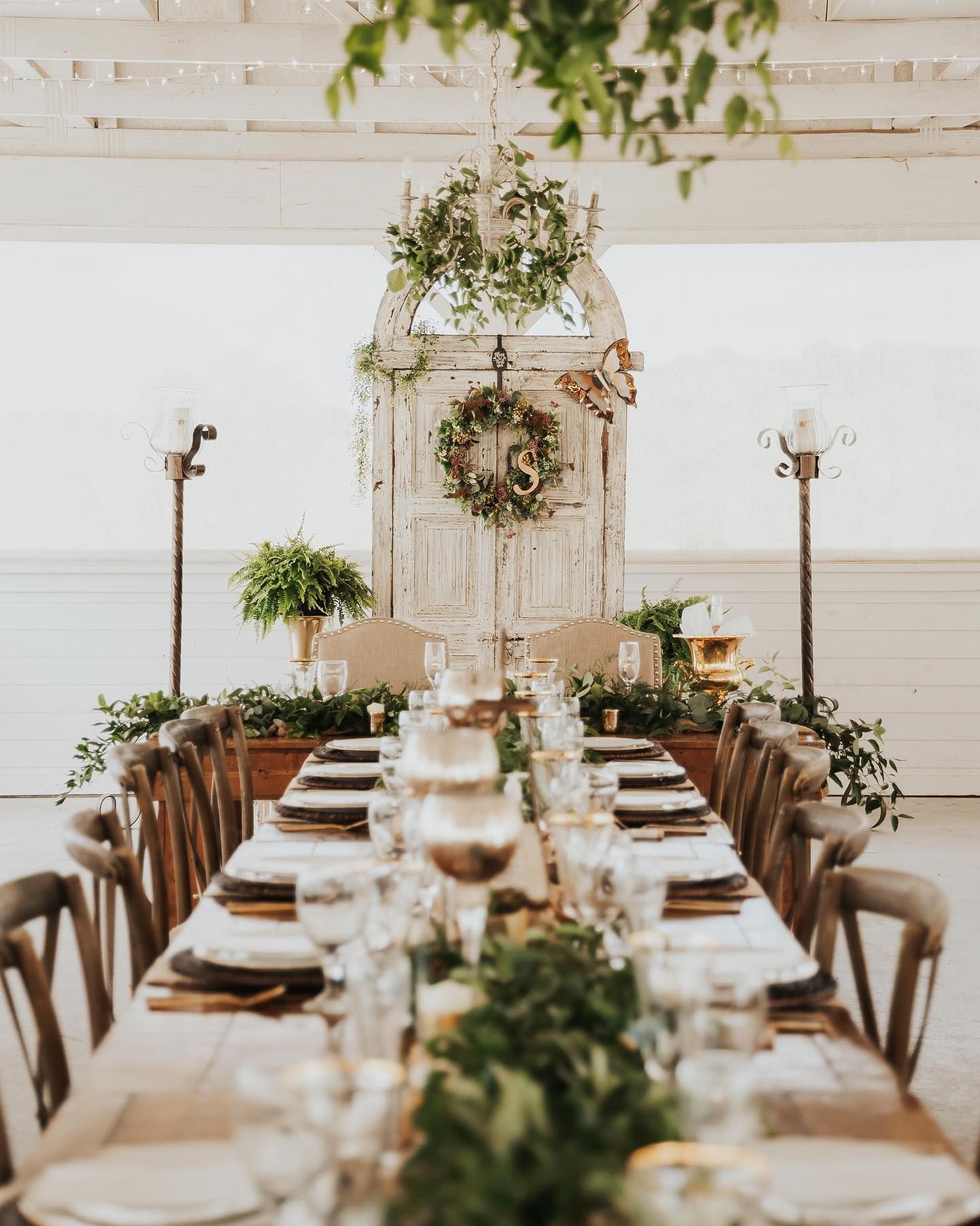 Long wooden table set for a wedding reception, with a decorated doorway backdrop.