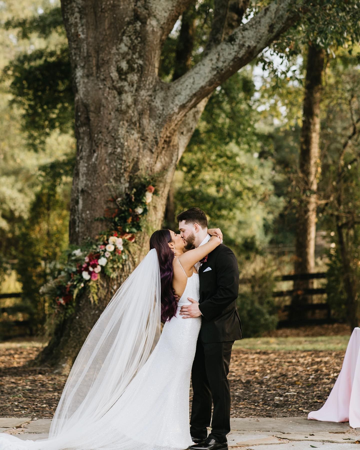 Couple kissing in front of a tree decorated with flowers; wedding ceremony.