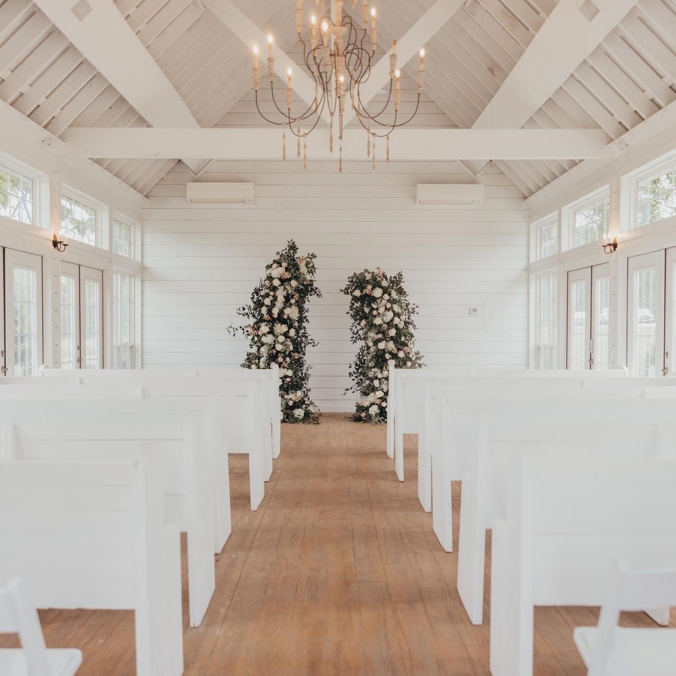 White wedding chapel interior with floral archway and rows of white benches.
