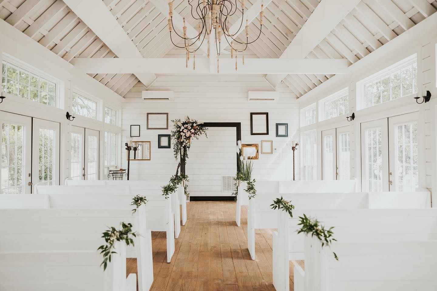 White wedding chapel with pews, floral arch, and framed art.