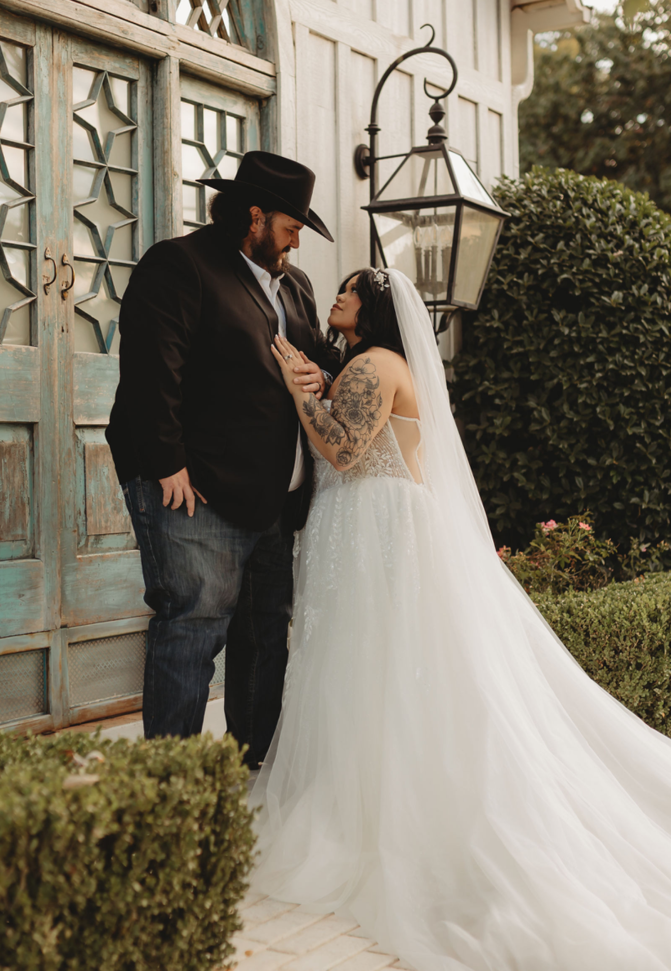 Bride and groom gazing at each other on wedding day. The bride wears a veil and gown, the groom wears a hat and blazer.