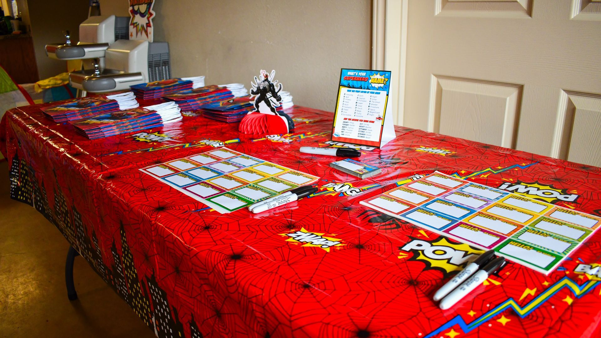 Red table with comic book theme tablecloth and supplies, including labels and markers.