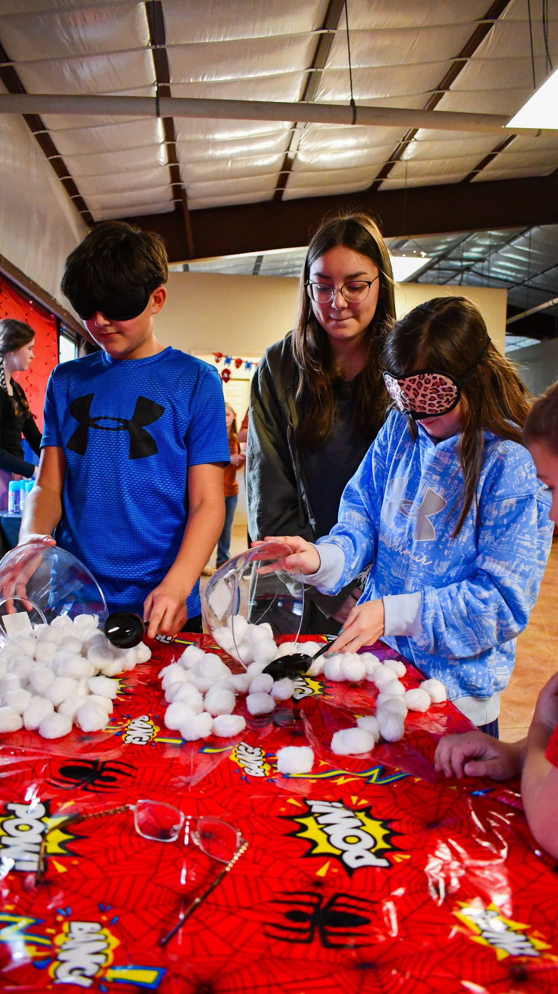 Children with blindfolds play a game, trying to grab cotton balls from a table.