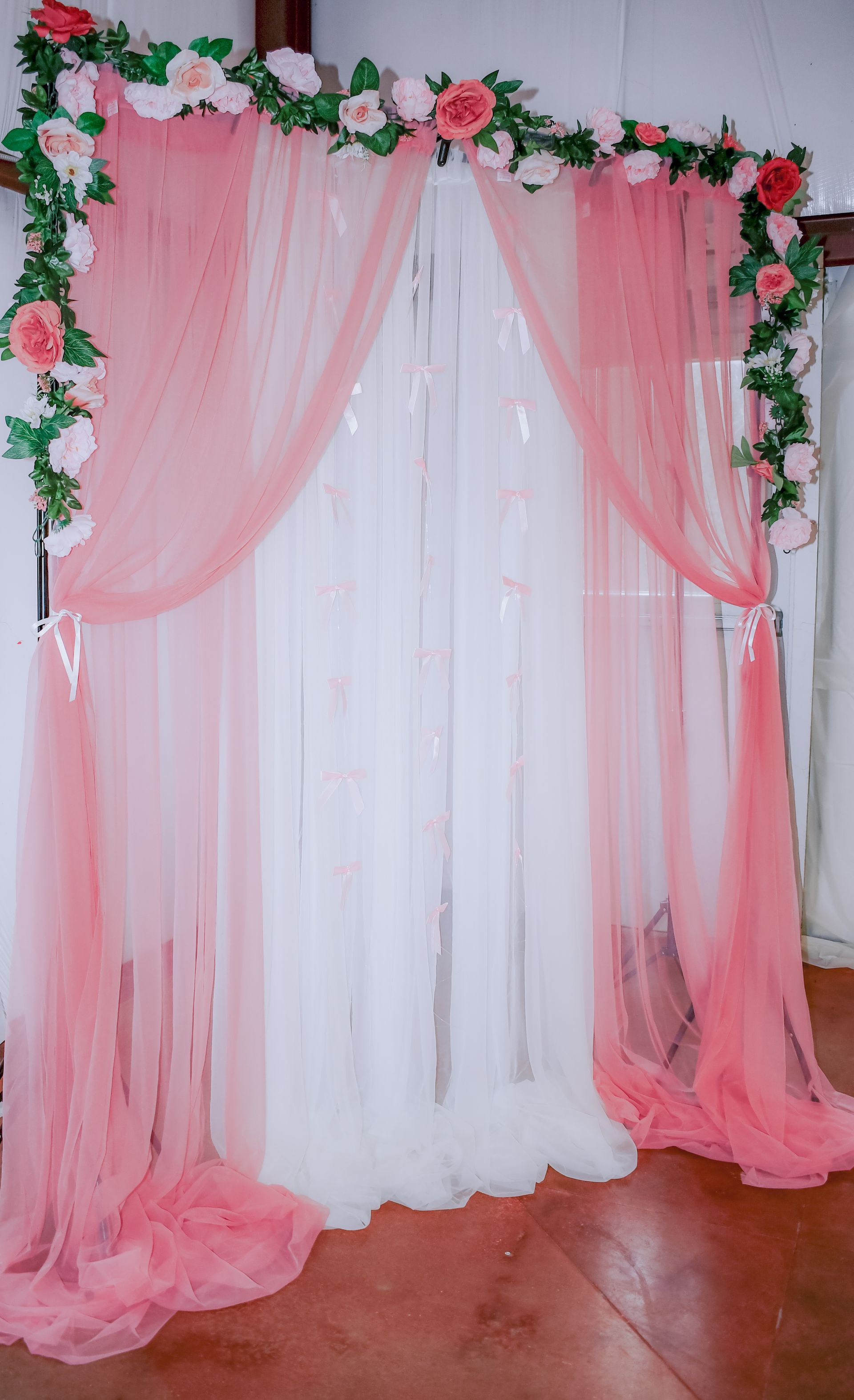 Pink and white tulle backdrop with floral garland, for a wedding or event.