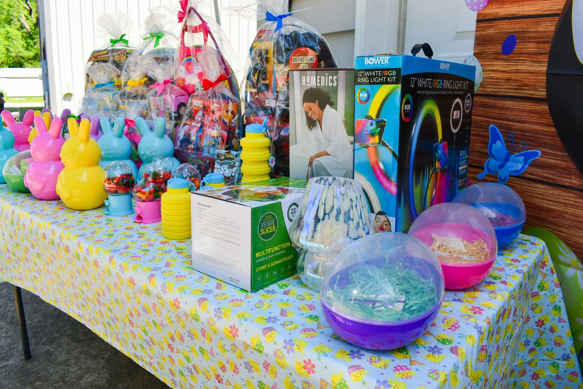 A table with Easter baskets, toys, and decorations in various colors set up outside.