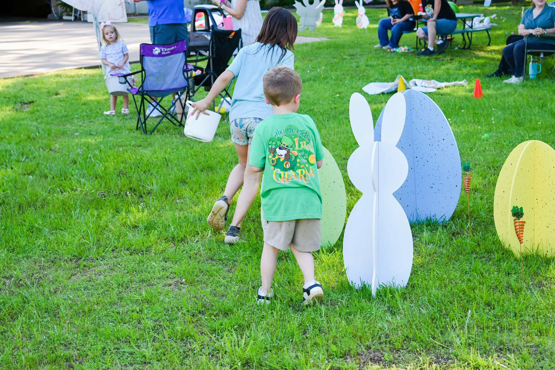 Children running on a lawn during an Easter egg hunt, with oversized cardboard Easter decorations.