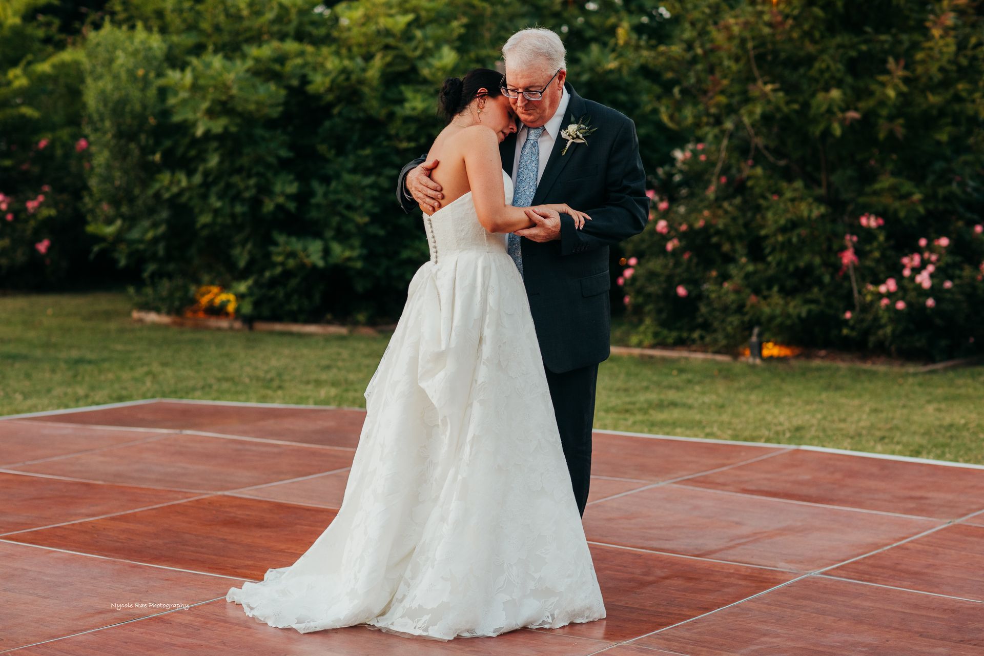 Bride in white gown dances with a man in suit on a dance floor, outdoors.