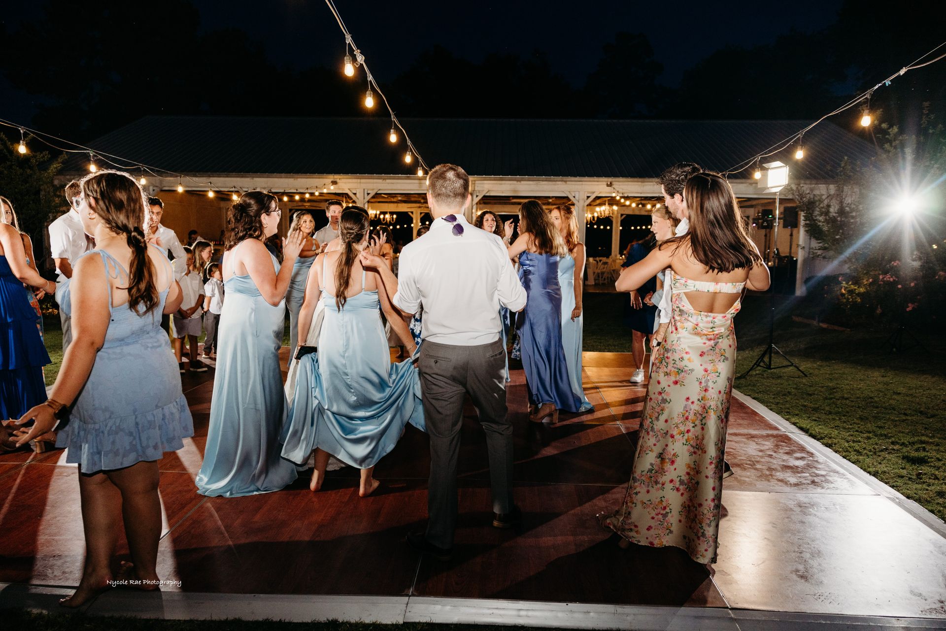 People dancing on a lit dance floor at an outdoor wedding reception at night.