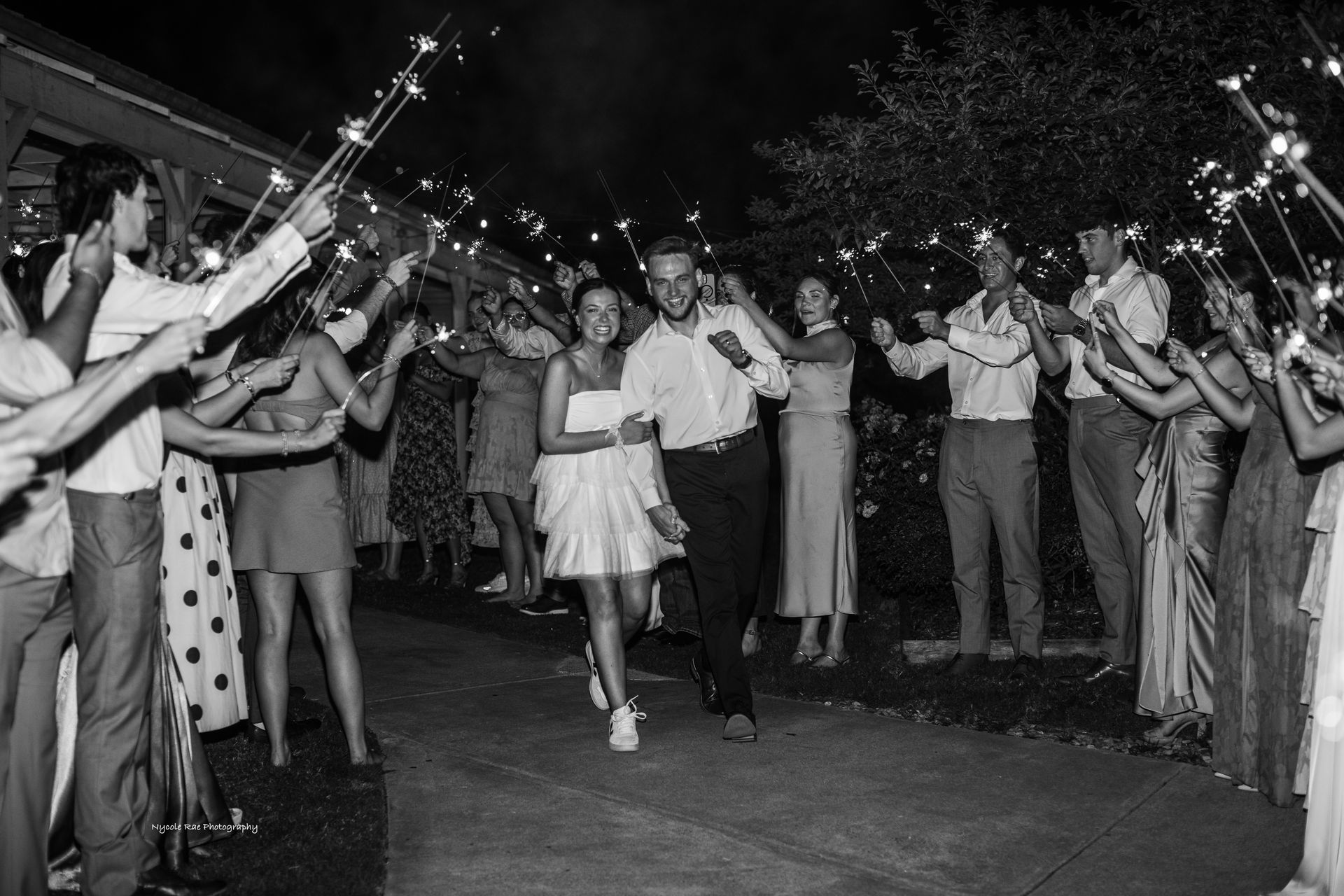 Couple runs through a sparkler exit at night, surrounded by guests with lit sparklers.