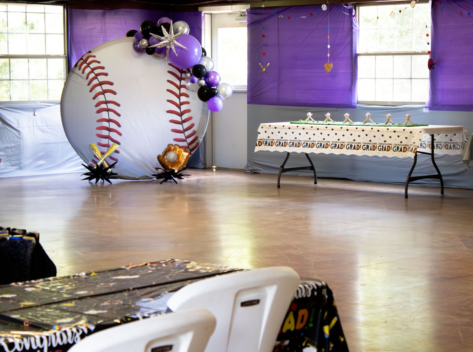 Baseball-themed party decorations: large baseball balloon, purple balloons, tables, and purple wall coverings.