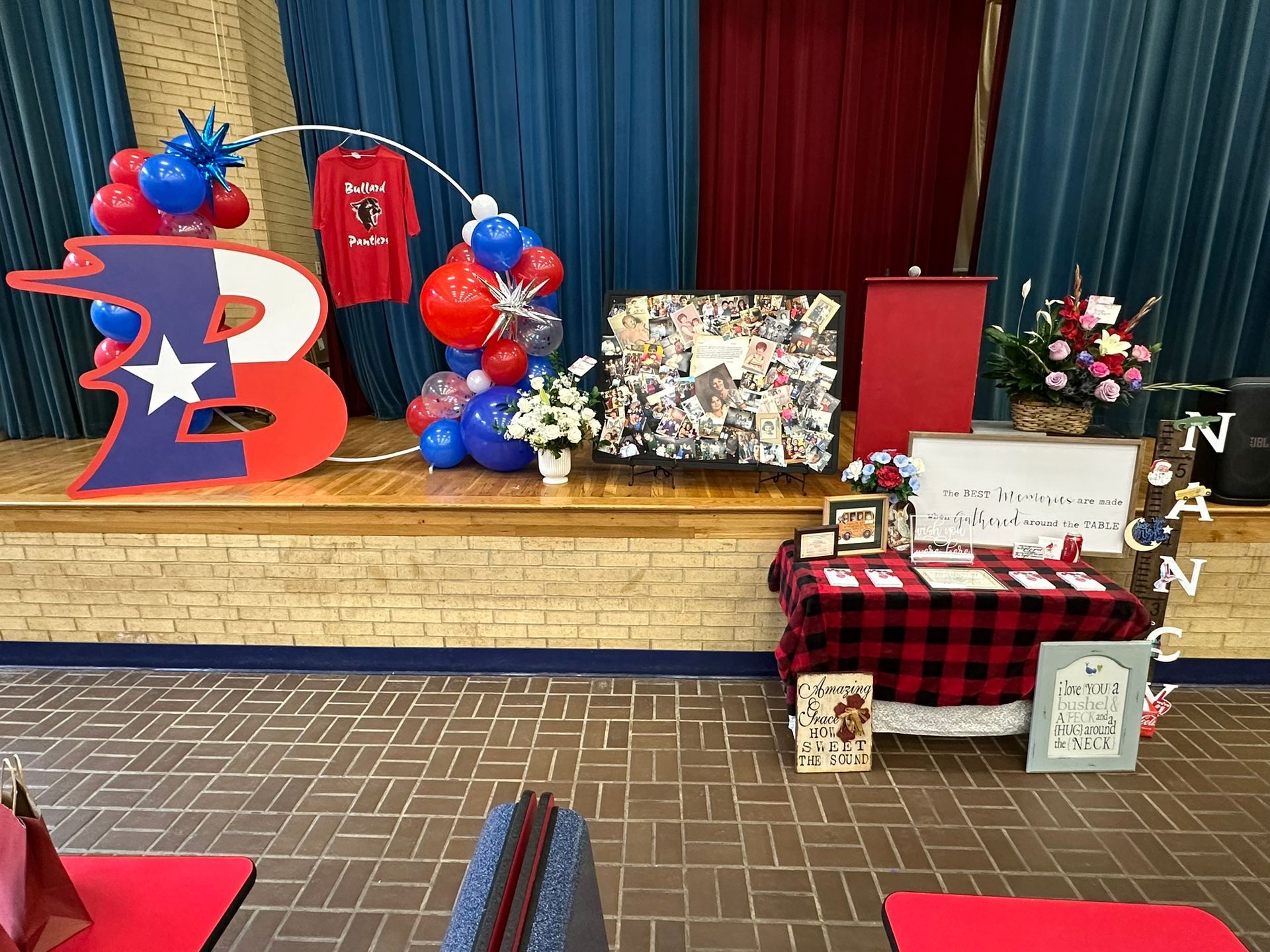 Decorated stage with red, white, and blue balloons, and a table covered in a red and black checkered cloth.