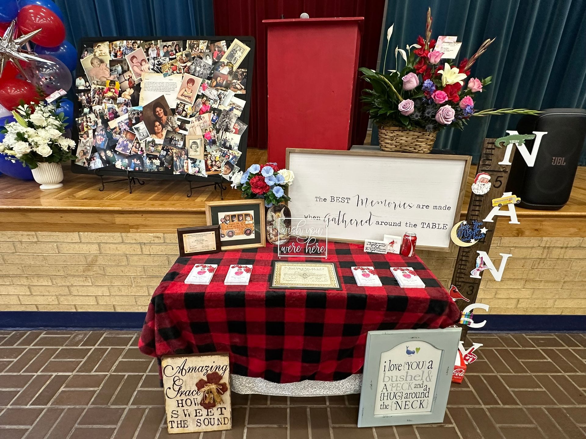 Display table with red and black checkered cloth, photos, and floral arrangements on a stage.