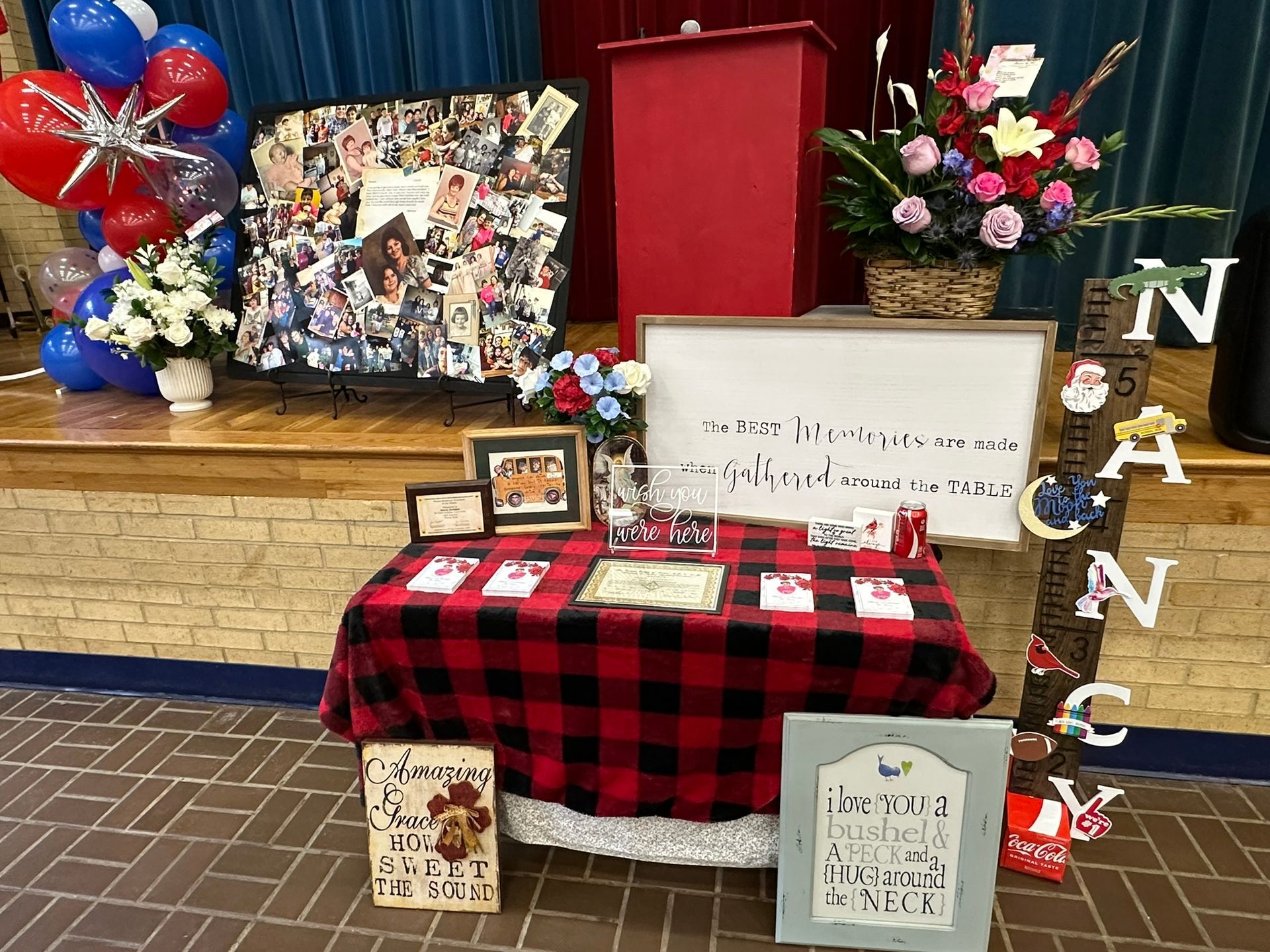 Display with photos, flowers, balloons, and gifts on a decorated table. The word 