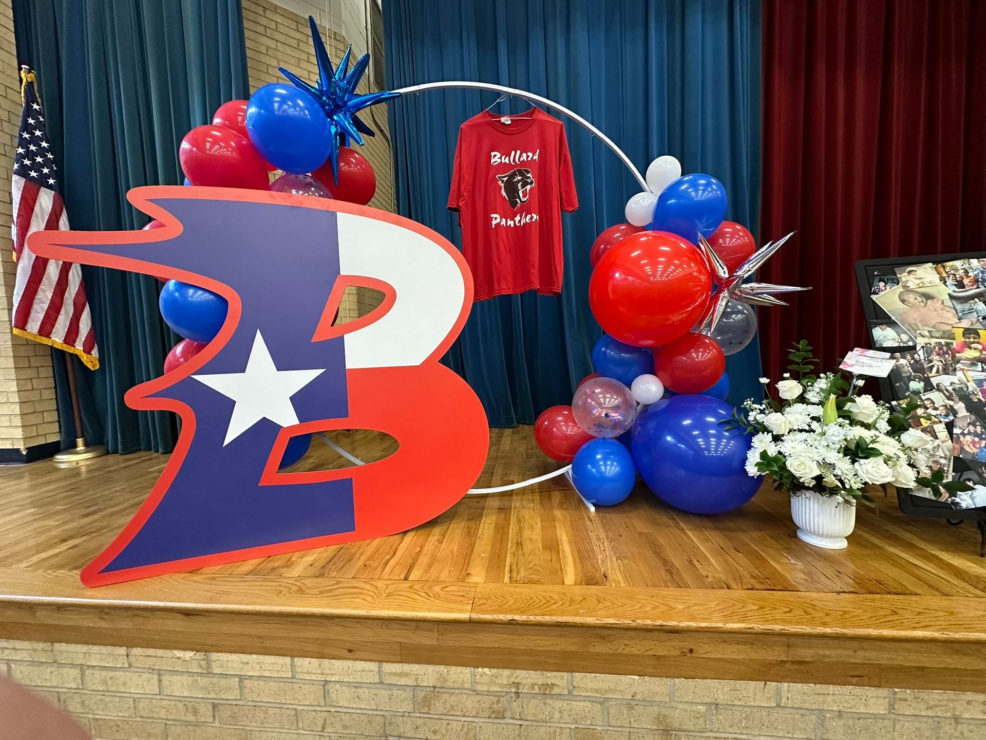 A stage decorated with red, white, and blue balloons, a Texas flag, and a school logo.