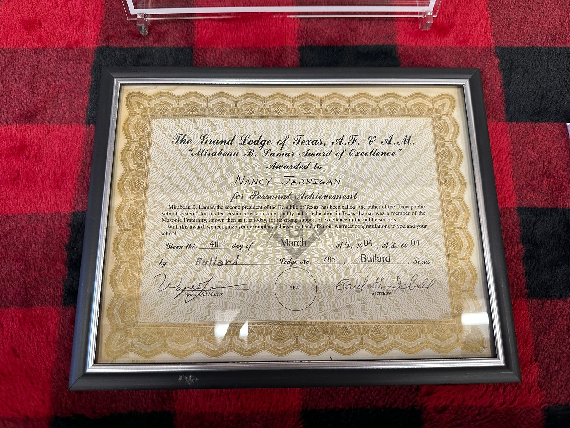 Framed Masonic certificate on a red and black plaid surface; gold trim and intricate script.