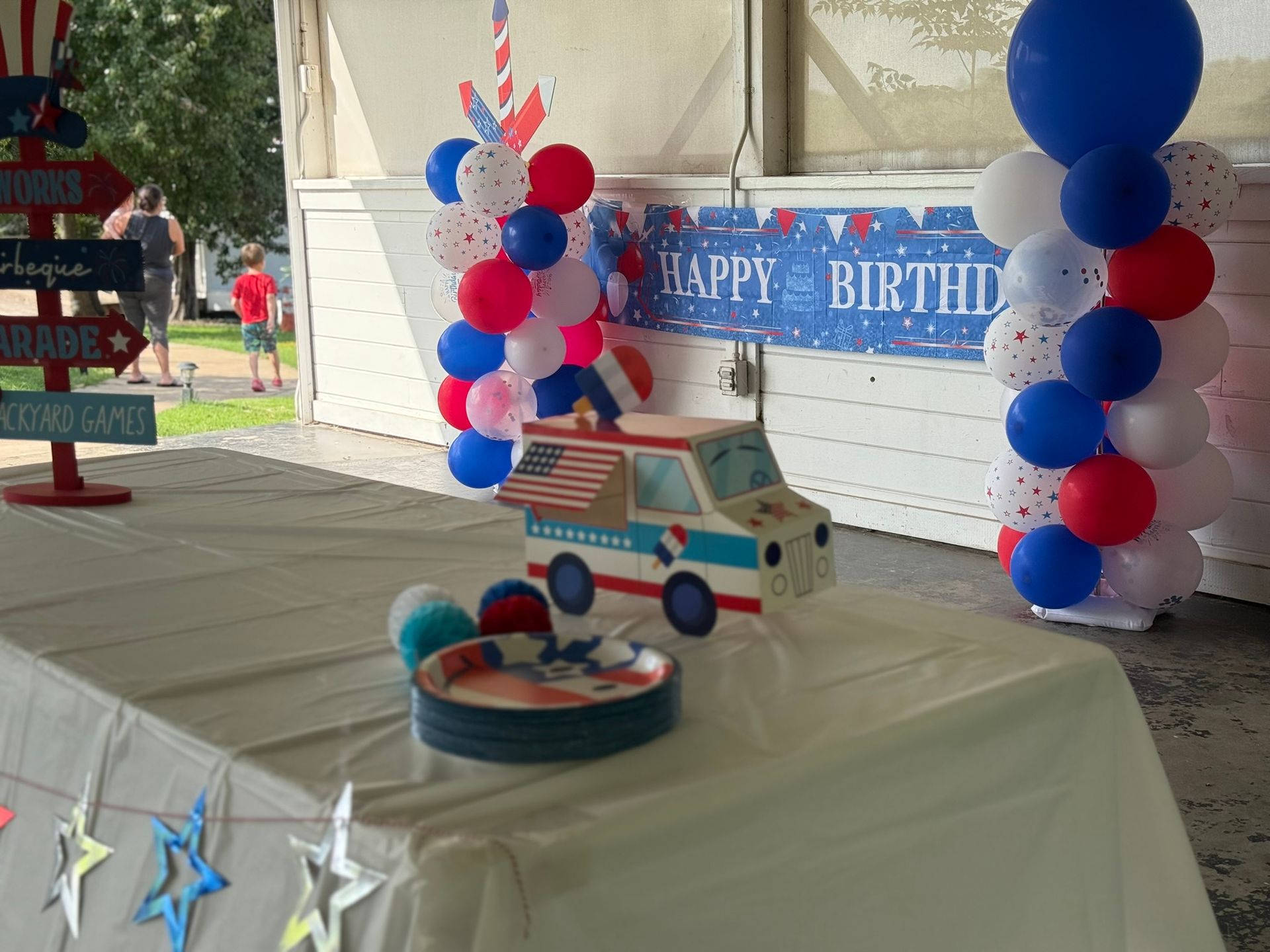 Festive birthday party table with red, white, and blue decorations, including balloons and an ice cream truck centerpiece.