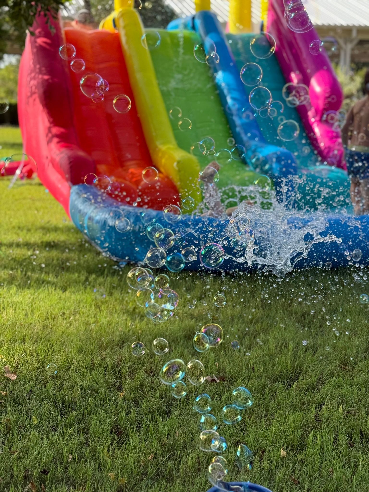 Colorful inflatable water slide with bubbles and splashing water on a grassy lawn.
