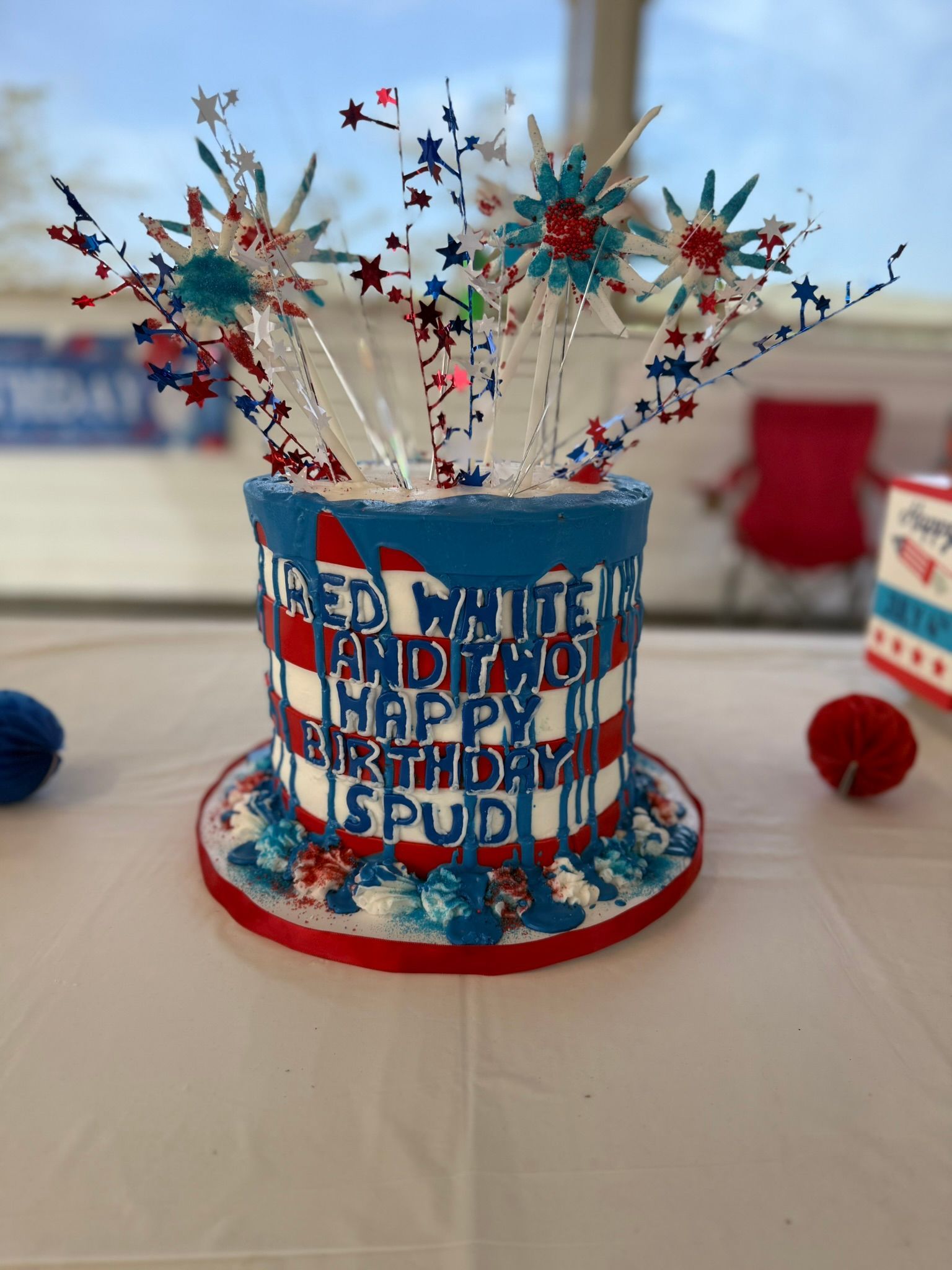 Patriotic cake decorated with red, white, and blue, topped with starburst decorations for a birthday.