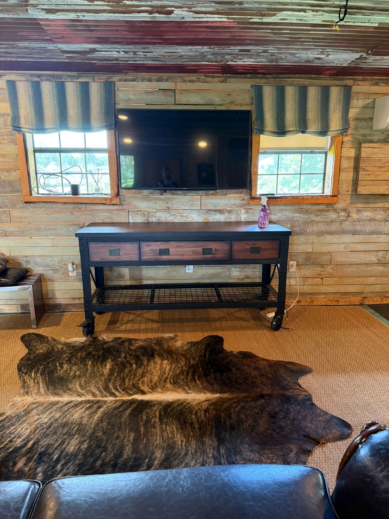 Living room with TV above a wooden console, cowhide rug, and window treatments.