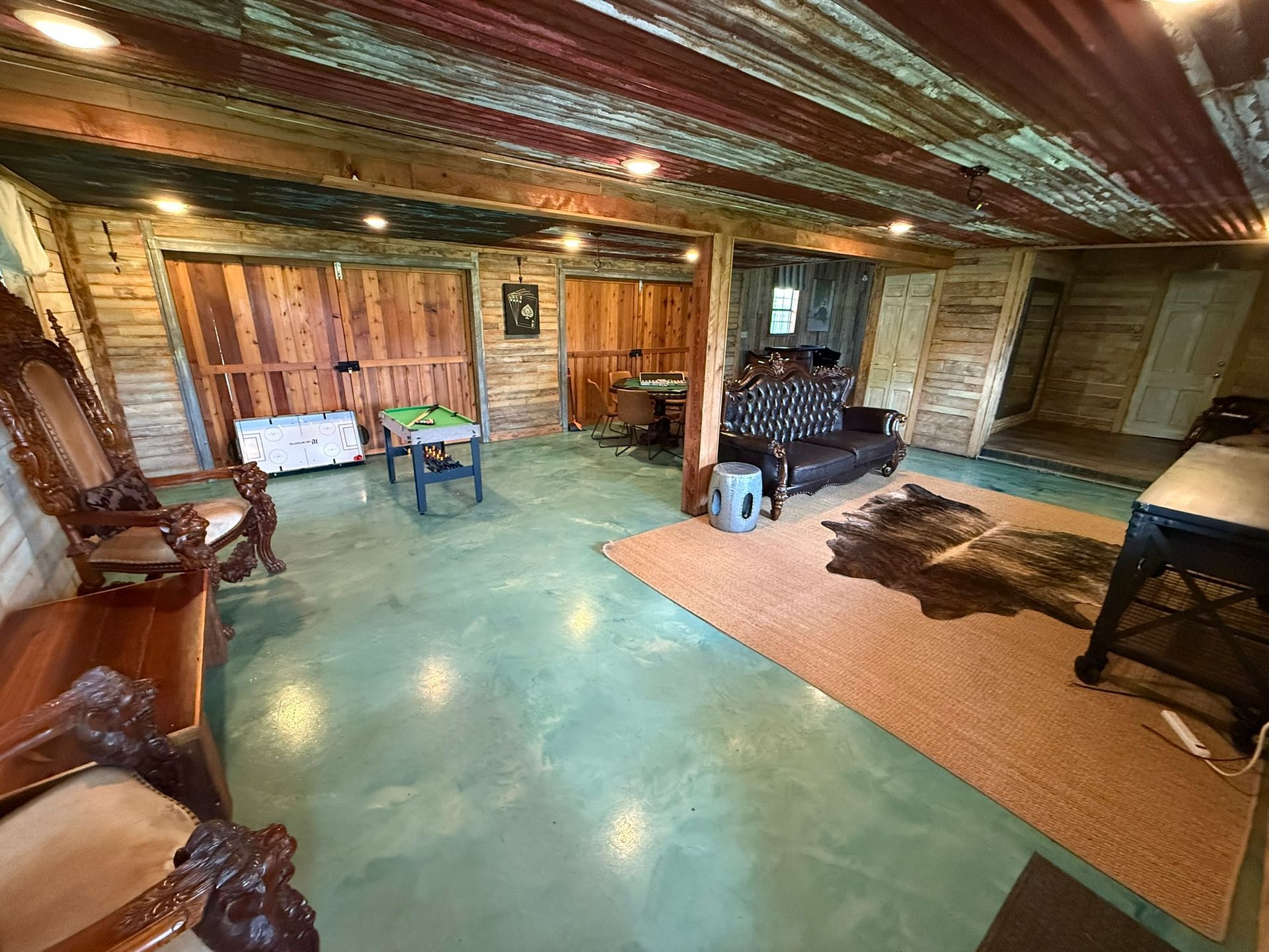 Rustic interior: wood walls, tin ceiling, concrete floor. Furniture includes sofa, ornate chair, rugs, and tables.