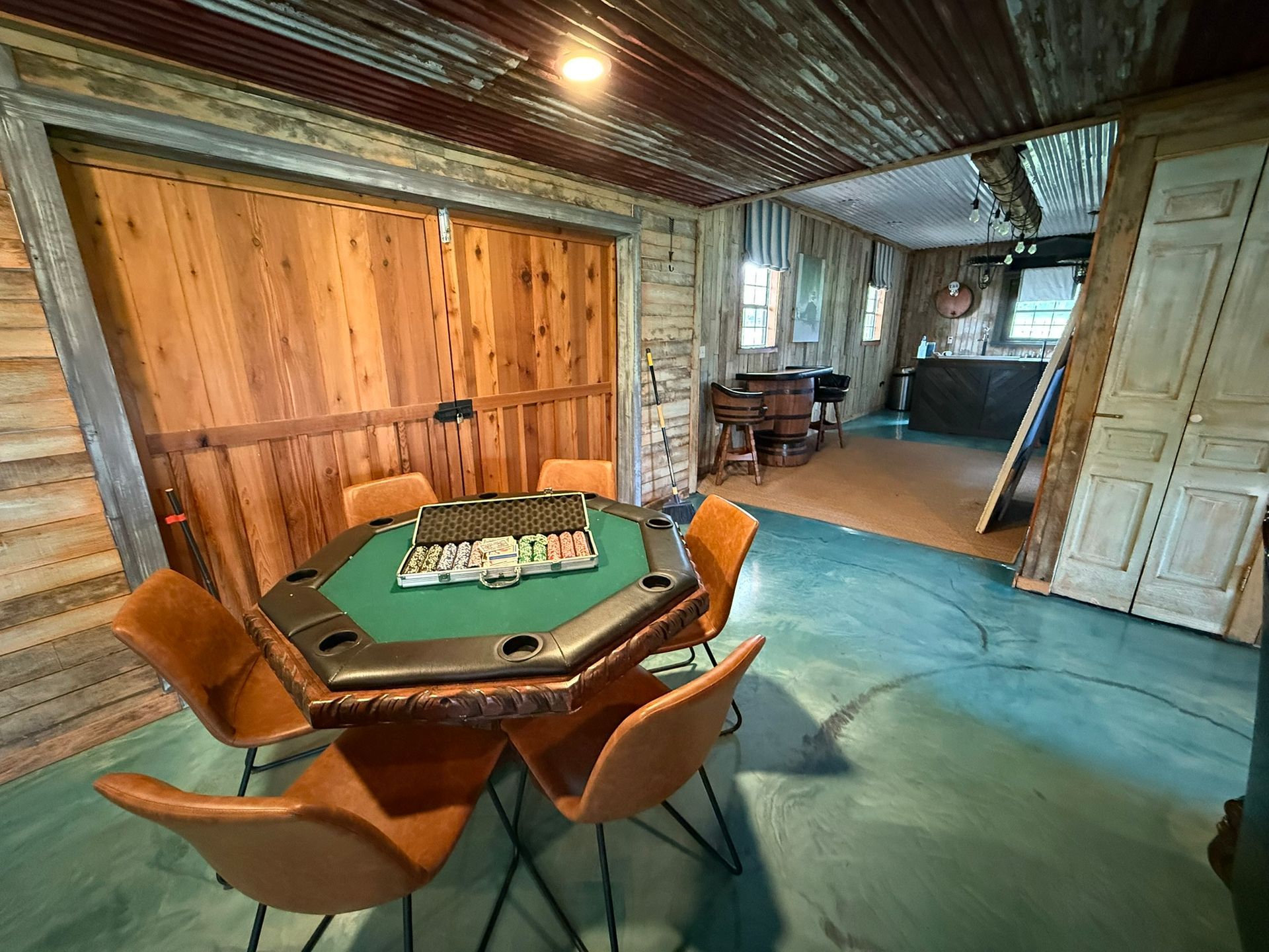 Poker table in a rustic room. Brown wood walls, green felt table, orange chairs.