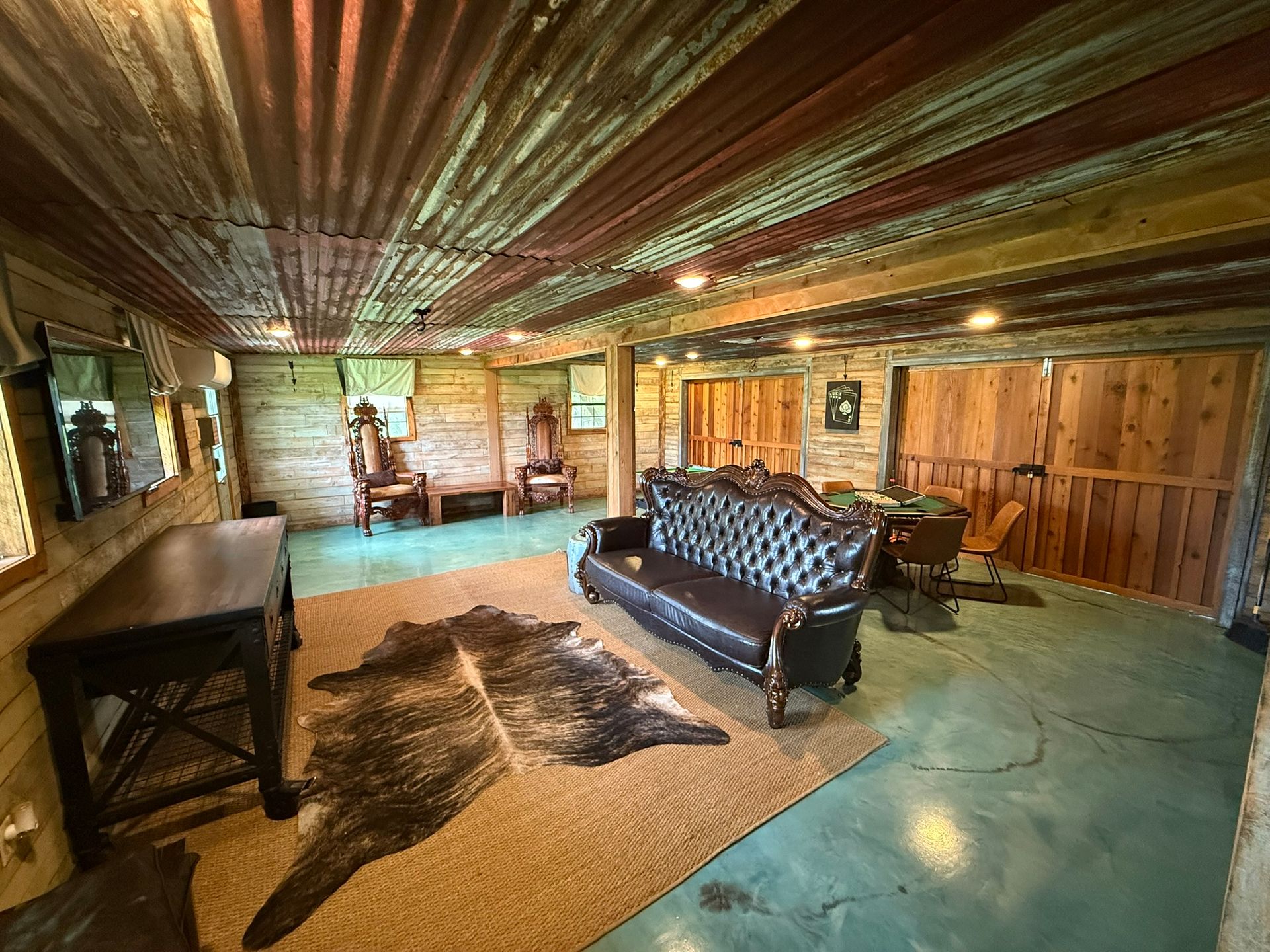 Rustic living room with leather couch, cowhide rug, wood paneling, corrugated metal ceiling, and dim lighting.