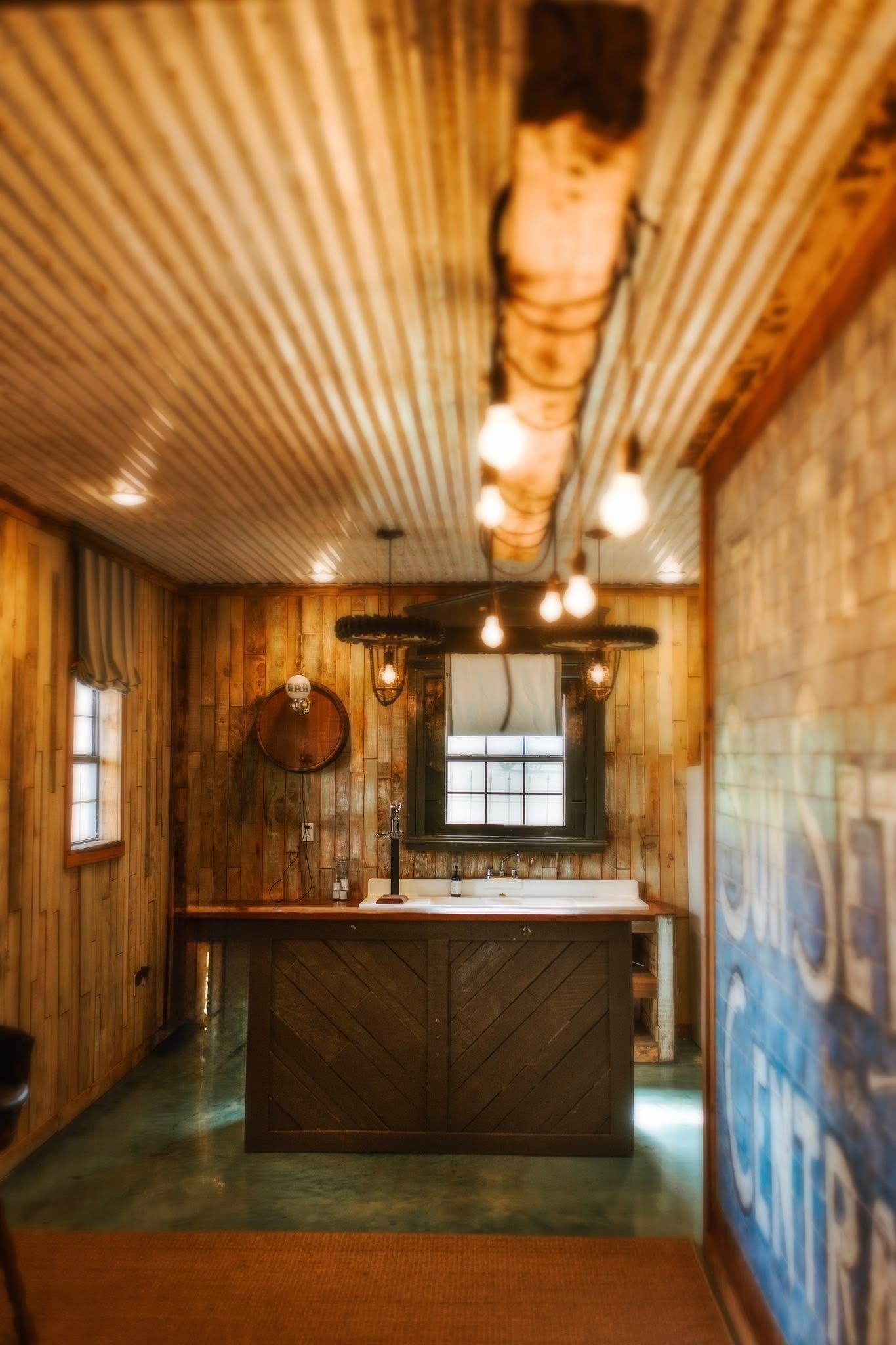 Rustic bar interior with wood paneling, corrugated metal ceiling, and hanging lights.