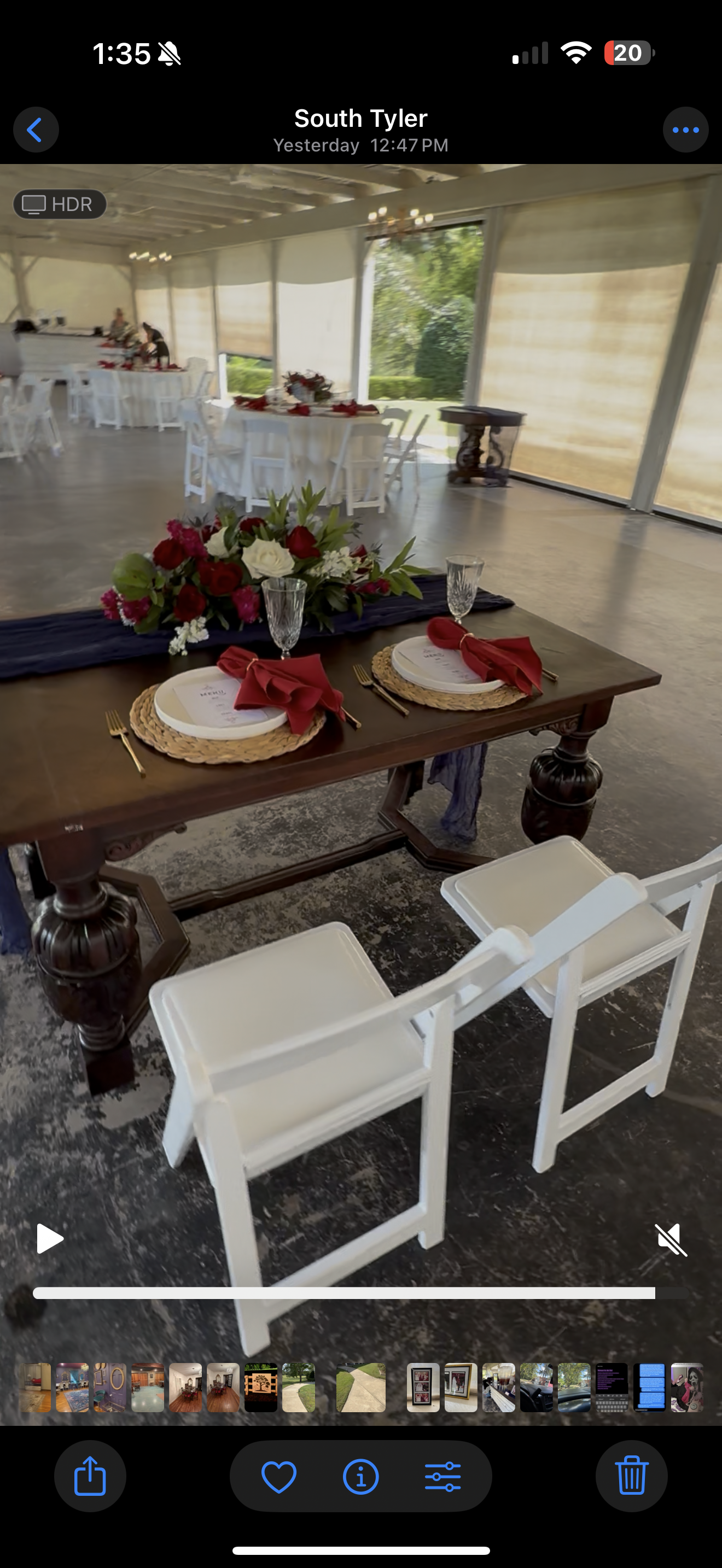 A wedding reception setup. A decorated table with two white chairs in front of an empty room with other tables.