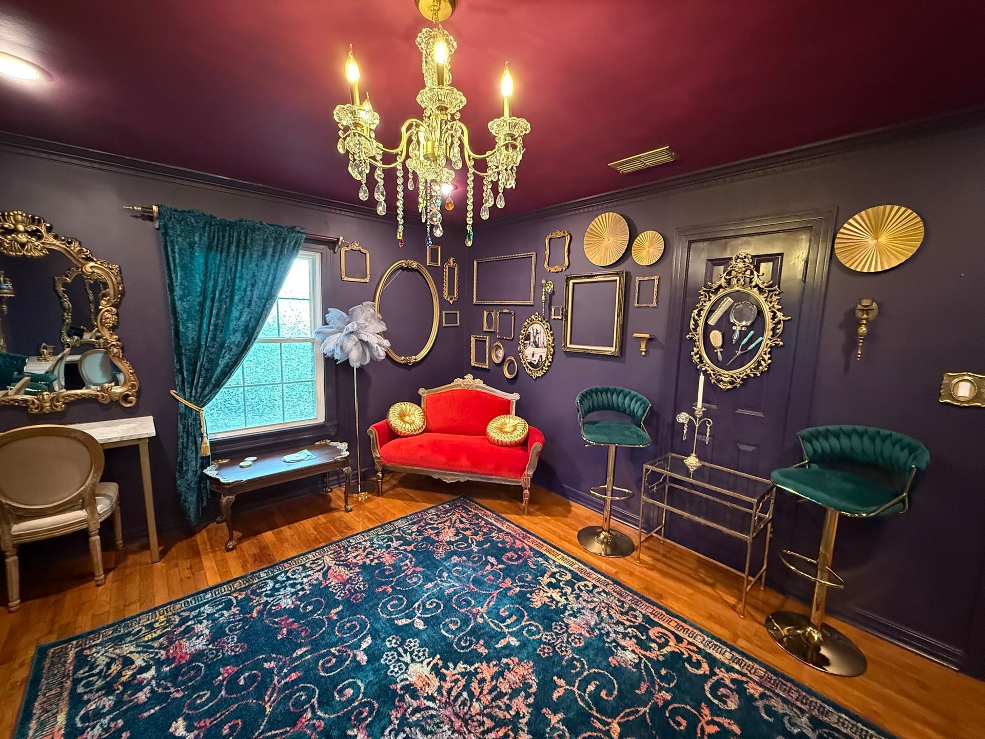 Elegant room with a red settee, teal accents, ornate gold mirror, purple walls, and a chandelier.
